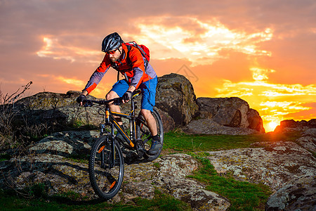 赛车手在美丽的日落山边骑着 极具活力的运动和冒险概念 的自行车下春落雪山速度竞赛乐趣岩石成人头盔天空运动员骑士活动图片