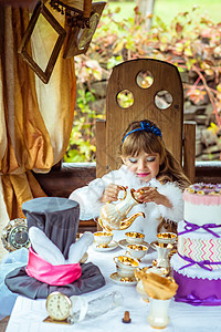 一个小美少女的前视 出现在爱丽丝在奇幻之地的风景中 把茶倒到桌子上的一个杯子里女性魔法蛋糕乐趣帽子童话戏服游戏仙境衣服图片