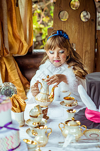 一个小美少女的前视 出现在爱丽丝在奇幻之地的风景中 把茶倒到桌子上的一个杯子里文化魔法仙境想像力快乐公园帽子童话裙子乐趣图片