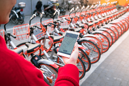 一个年轻女人正在寻找智能手机 找她的自行车快乐女性街道娱乐成人衣服城市冒险乐趣骑术图片