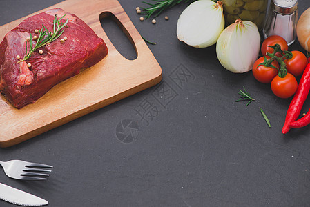 切菜板上生牛肉 配有香料和原料绿色鱼片黑色牛扒红色胡椒迷迭香食物木板小腿图片