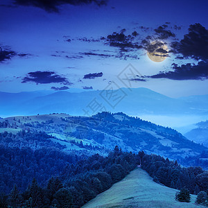 深夜在山坡陡峭的森林中蓝色旅游远足荒野树木薄雾云杉草地爬坡月亮图片