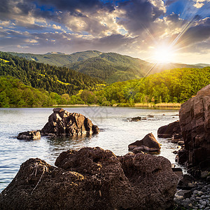 日落时山上森林附近带石块的湖边湖岸图片