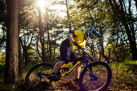 黄色T恤和Helmet在森林中骑自行车的职业赛车员名单 极端运动概念山地车踪迹运动员车轮骑士森林安全头盔耐力漂移图片