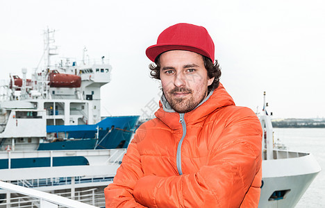 一名在背景海陆山上成功的年轻男子的肖像橙子夹克假期成人海洋海岸码头海浪码头工人天空图片