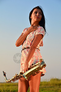 美丽的女孩手里握着萨克斯风音乐家女性萨克斯手姿势黄铜运动身体假期音乐艺术家图片