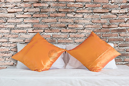 白床上的古老红砖墙和橙色枕头图片