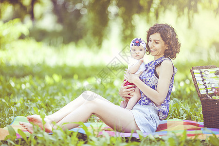 年轻美丽的母亲坐在公园的毛毯上与女儿坐在一起野餐季节婴儿食物快乐女性家庭篮子幸福女士图片
