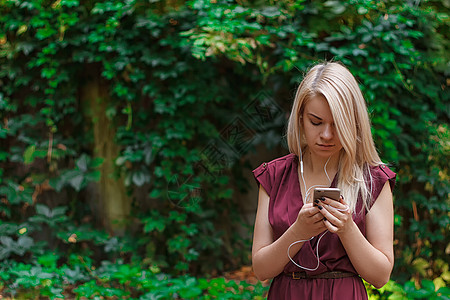 年轻有吸引力的女人正在用她的智能手机发短信公园互联网快乐微笑女孩女士电话花园长发金发女郎图片