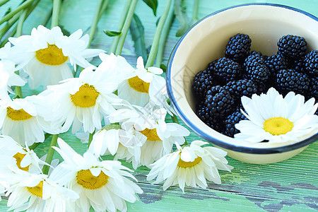 碗里有美味的新鲜黑莓和鲜花洋甘菊蓝色浆果黄色花朵白色图片
