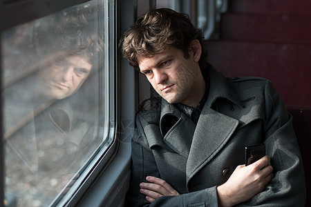 乘火车旅行 悲伤的男人乘火车旅行 透过窗户望着窗外 想着单相思 捏着手里的电话 独自一人坐在空荡荡的火车车厢里 真人系列小伙子青图片