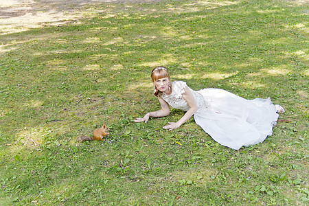 白新娘躺在松鼠旁边的草地上蕾丝刺绣金发女士新娘裙子眼睛头发丝绸微笑图片