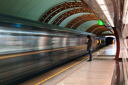 孤独的年轻人 在地铁站用智能手机拍了照片 背面模糊移动列车图片