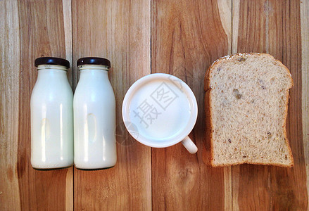 以木制背景的奶瓶和牛奶杯装面包切片图片