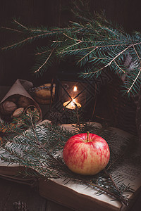 圣诞树枝上的红苹果和黄苹果 还有一本旧书 在黑灯笼或蜡烛手旁边 有灯光燃烧图片