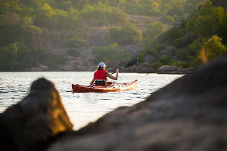 年轻女子在美丽河流或山湖上划红卡雅克(Red Kayak)图片