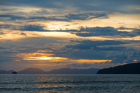 美丽的乌云和橙色的日落 在海面上 山峰在图片