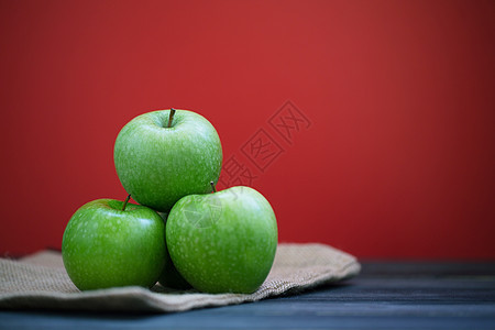 一群绿色苹果 在木桌和红色背景的麻袋上新鲜而绿苹果图片