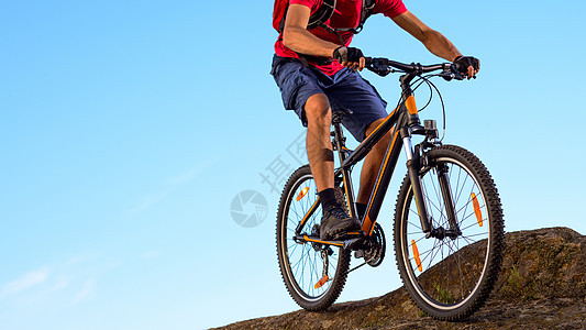蓝天背景的 红色骑车在岩石下沉 中的赛车选手 极端运动和概念踪迹行动山地车自行车运动员乐趣下坡耐力赛冒险活动图片