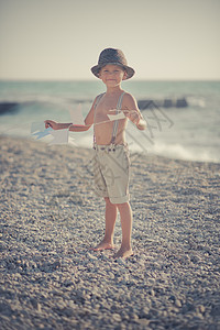 可爱的老式男孩在沙滩上散步 穿着花哨的短裤 戴着绞刑架和绅士帽 带着锚在令人敬畏的海洋上独自享受夏日时光 童年生活的可爱场景美德图片