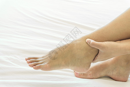 妇女手握脚踝 在白床 保健护理和扭伤肌肉疾病身体药品女性痛苦边缘治疗卧室图片