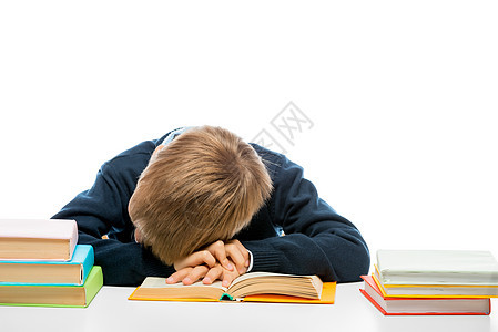 一个疲累的在校男孩在桌子上看书时睡着了图片