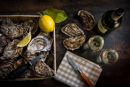 生生牡蛎篮子 木板上加柠檬 酒瓶和玻璃壳类熟食石头黑色海鲜石板盘子食物美食奢华图片