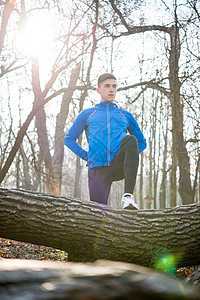 健康的生活方式和运动概念 年轻男性跑步者在寒冷的阳光秋天早晨公园展展木材日志男人闲暇活动训练蓝色晴天踪迹运动员图片