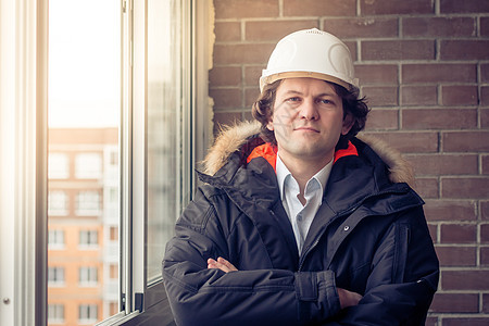工程师穿戴白色安全头盔的肖像 在建筑工地用砖底交叉他的手臂 软焦距 刻着图片
