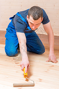 熟练的青年工人在房子里木地板上涂彩滚滚图片