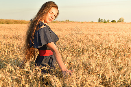 一名年轻女子站在阳光下的小麦田中图片
