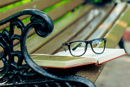 一个开放的书和眼镜 躺在公园的长椅边缘图片