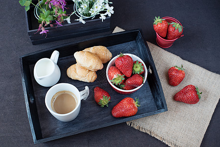 黑桌上木盘上的咖啡 小法国糕点和草莓 白花和紫花放在装饰的木箱中 黑色背景午餐食物咖啡店面包早餐浆果照片盘子甜点杯子图片