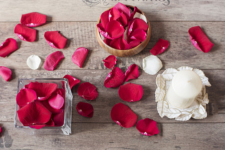 玫瑰香装满红玫瑰花瓣 白色芳香香香草蜡烛的玻璃花瓶和木弓 木质背景 阿罗马疗法概念背景