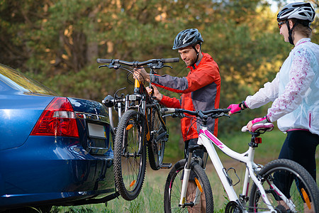 冒险与家庭旅行概念 由Bike Rack在汽车上搭乘的  年轻夫妇脱身山车男人蓝色森林车辆女性自行车车轮山地车头盔载体图片