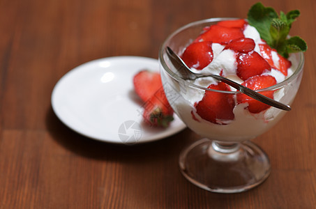 带勺子的玻璃碗里放着草莓片和薄荷叶的香草冰淇淋图片