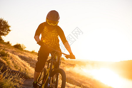 赛车手骑着山上摩托 在夏日落石轨的夜晚 极端运动和Enduro自行车概念太阳活动乐趣山地车护目镜爬坡下坡眼镜车轮踪迹图片