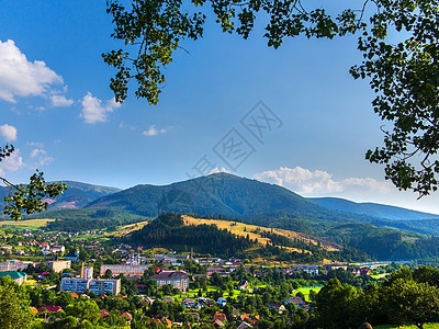 夏日城市的美丽风景躺在山谷中 背景是黄色的小麦坡和长满绿色森林的山峰图片