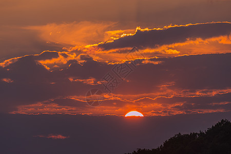 夜空的美丽景观 太阳的红色圆盘 坐在云层上 俯视着树的顶部 看得见图片