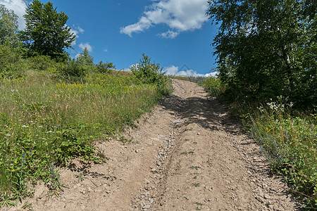 在两岸绿树的背景下 沿陡坡行走的山地灰尘横扫的公路图片