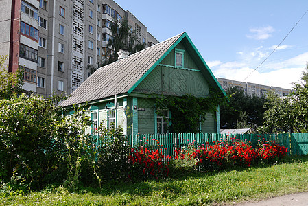 一座木制乡间别墅 涂有油漆 木栅栏 种植在靠近多层城市住宅的鲜花前图片