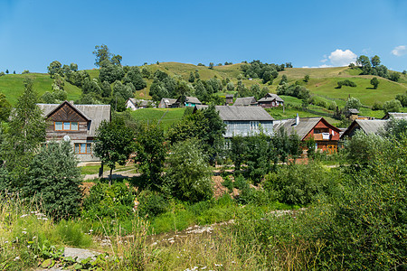 一个村庄 在一座绿色山和一片蓝天的背景下 有两层棚屋和小房子;图片
