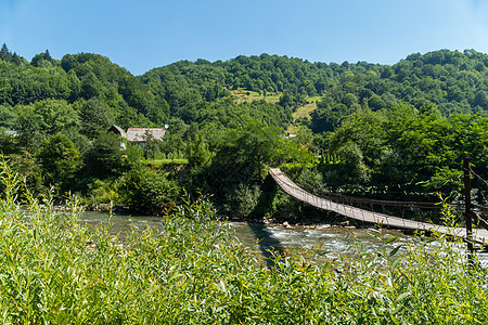 一条跨越山河的行人桥 通向位于对岸 树木绿化处的农村房屋和林木旁图片