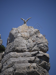 蓝天下高陡峭的岩石上的鹰雕像图片