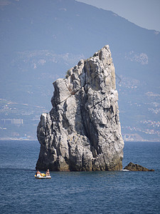 在远处一个大型度假小镇的背景下 蓝色大海中间的一块陡峭的小岩石图片