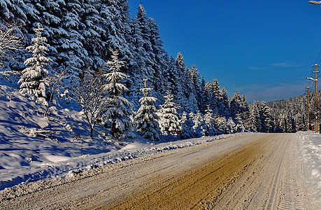 寒冷的冬天风景 在雪覆盖的斜坡上生长着一条沿着美丽的高山壁运行的滚动道路图片