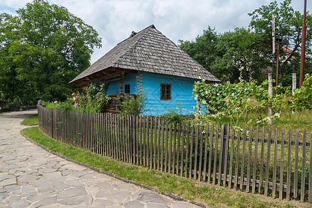 一座美丽的房子 墙壁漆成木头 站在木板栅栏后面 院子里有绿色植物 旁边是铺着石头的街道图片