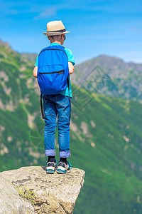 山上带着背包的男孩 站在岩石上 看着图片
