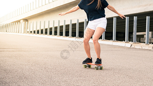 年轻美丽的金发女孩在桥上骑着明亮的滑板晴天运动橙子金发女郎滑冰溜冰者牛仔裤女性木板乐趣图片