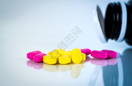 黄色和粉红色的椭圆形药丸 白色背景上有阴影 药瓶模糊 轻度至中度疼痛管理 止痛药 布洛芬胶囊丸图片